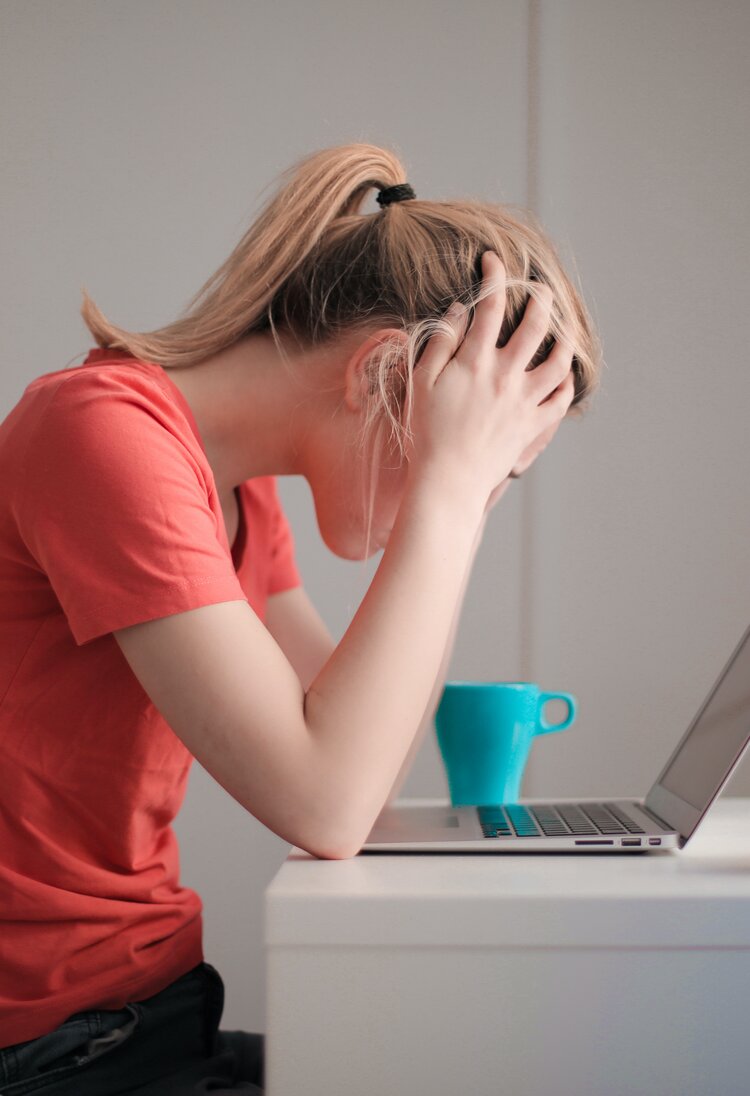 Eine Frau mit blonden Haaren und rotem T-Shirt sitzt vor dem Laptop und hat den Kopf auf die Hände gestützt. | © Pexels/Andrea Piacquadio