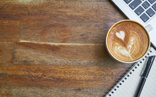 Auf einem braunen Tisch ist eine Tasse Kaffee, ein Notizblock und ein Laptop. | © pixabay