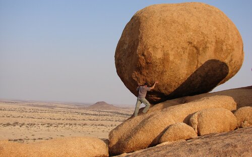 Ein Mann hält einen grossen Runden Felsen.  | © unsplash
