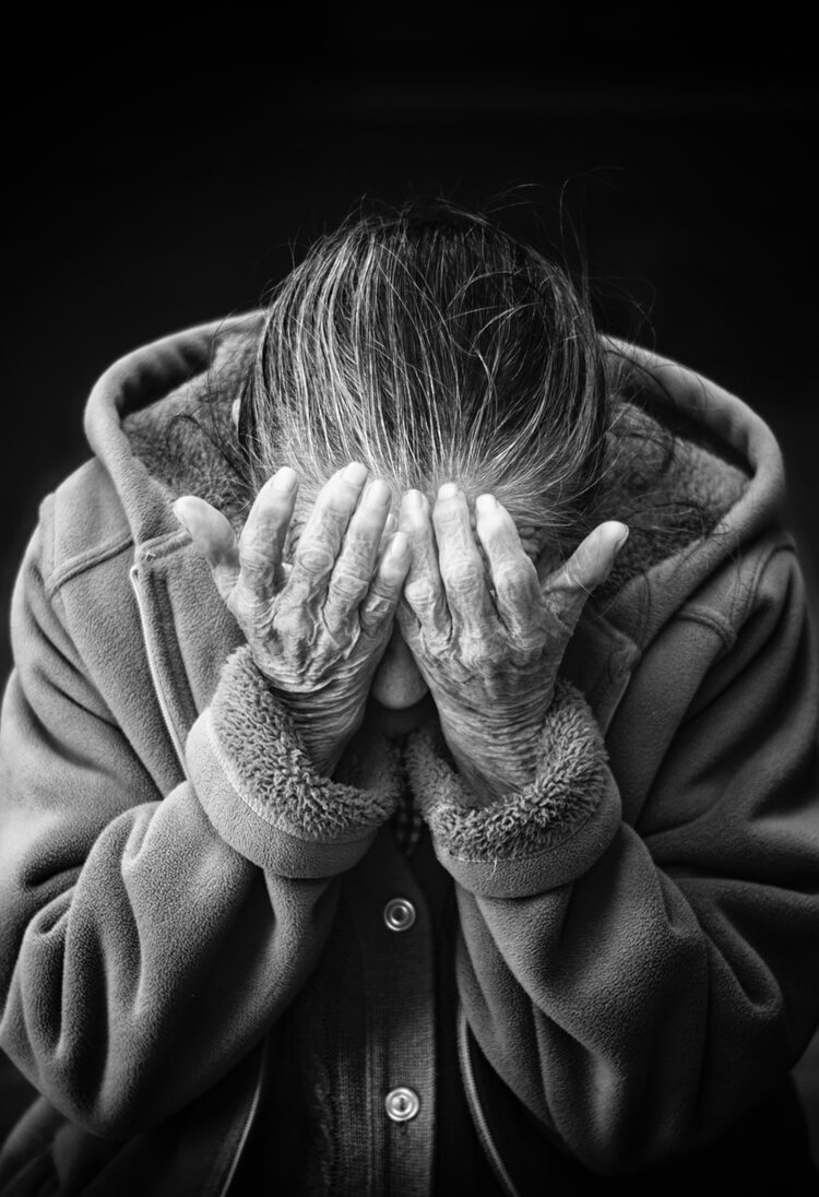 Alte Person hält Kopf nach unten und hebt Hände vors Gesicht. | © Unsplash