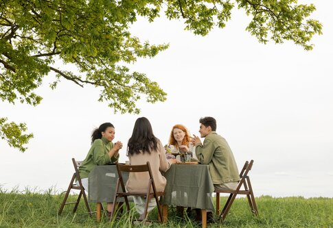 Ein Tisch im Grünen an dem vier Freunde sitzen und sich unterhalten. | © Pexels / Ron Lach