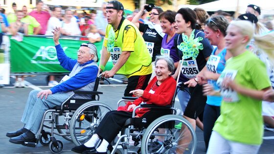 Firmenlauf mit zwei älteren Menschen im Rollstuhl, die von den Läufern gestossen werden. | © Pixabay