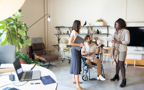 Drei Personen stehend im Büro, wobei eine Person mobilitätseingeschränkt ist. | © pexels