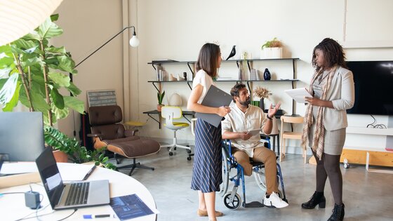 Drei Personen stehend im Büro, wobei eine Person mobilitätseingeschränkt ist. | © Pexels/Kampus