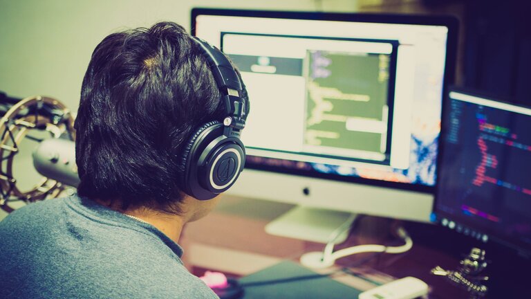 Ein junger Mann arbeitet konzentriert mit Kopfhörern vor dem Bildschirm. | © pexels