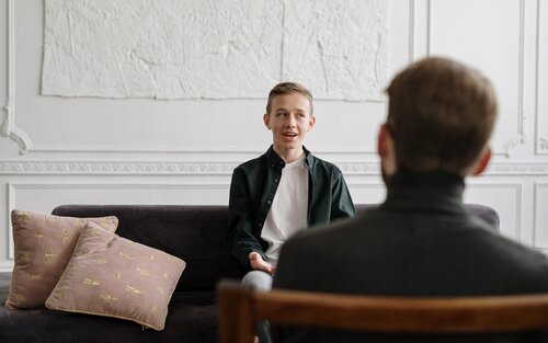 Ein junger Mann mit blondem Haar sitzt auf einem Sofa, ihm gegenüber ein ältere Mann mit Notizblock, der ihn coacht. | © pexels