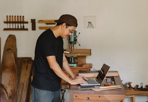 Ein Mann in einem Atelier arbeitet an seinem Laptop, der auf einer Werkbank steht. | © pexels