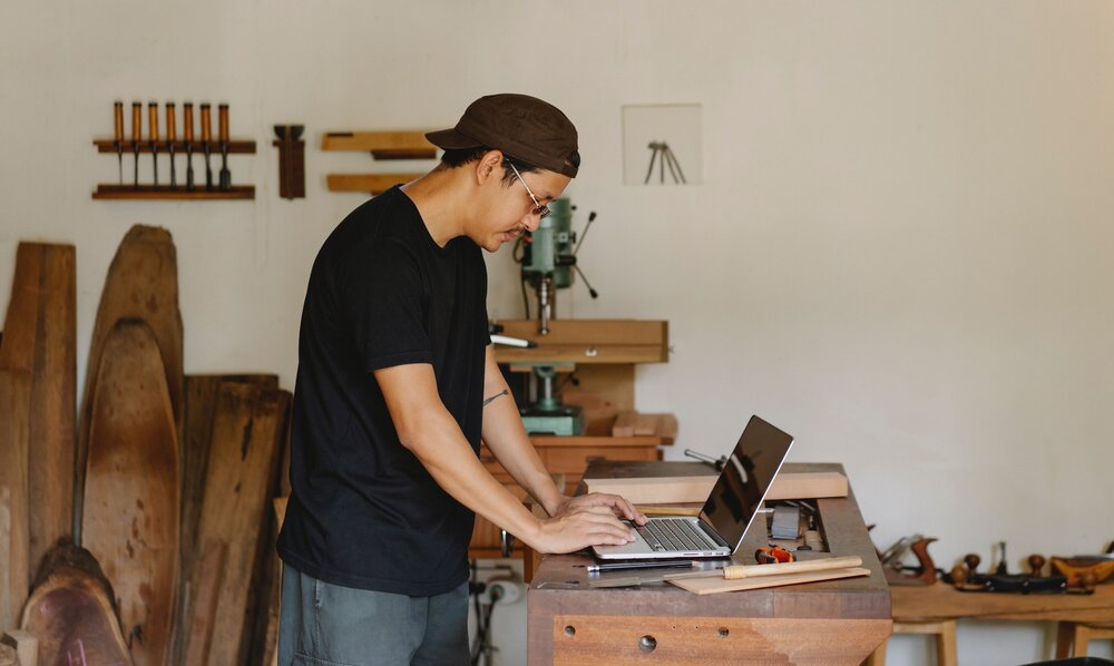 Ein Mann in einem Atelier arbeitet an seinem Laptop, der auf einer Werkbank steht. | © pexels
