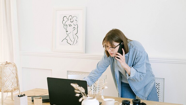 Eine Frau telefoniert mit dem Handy und schaut gleichzeitig etwas im Laptop nach. | © pexels