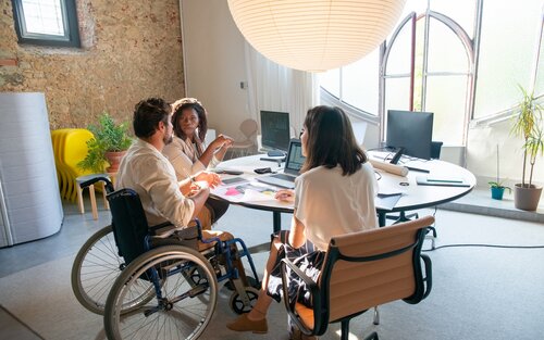 Ein Team von drei Personen, wobei eine im Rollstuhl sitzt, arbeitet gemeinsam in einem Sitzungszimmer. | © pexels