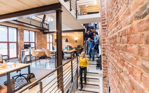 Modernes Büro mit schmaler Treppe rechts im Bild, auf der gerade verschiedene Personen gleichzeitig runter gehen. | © pexels