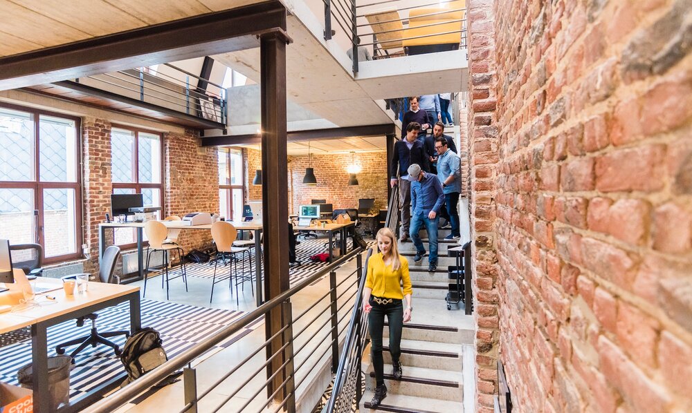Modernes Büro mit schmaler Treppe rechts im Bild, auf der gerade verschiedene Personen gleichzeitig runter gehen. | © pexels