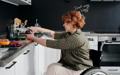 Eine Frau im Rollstuhl schneidet in der Küche eine Avocado auf. | © Pexels / Marcus Aurelius