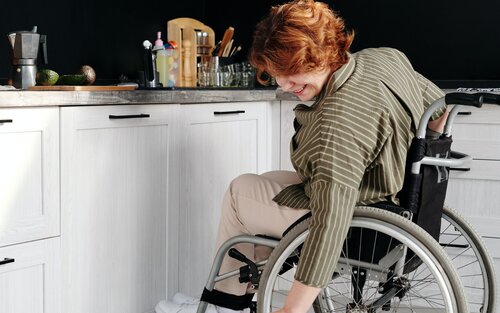 Foto einer Frau im Rollstuhl, die in ihrer Küche eine Katze streichelt. | © pexels