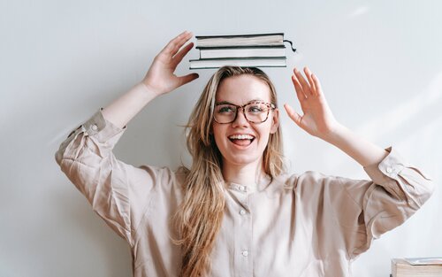 Une femme rit en tenant trois livres en équilibre sur sa tête. | © pexels