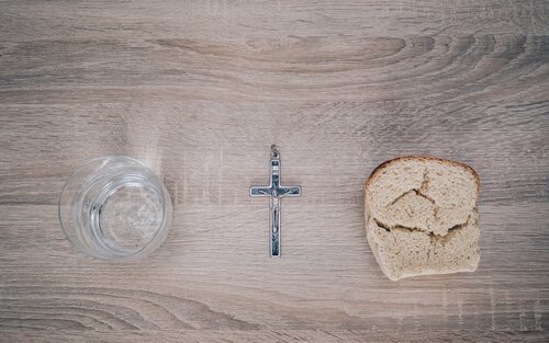 Ein Kreuz, daneben ein Stück Brot und ein Glas Wasser. | © unsplash