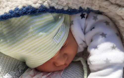 Zu sehen ist ein schlafendes Baby in einem weiß-blauen Strampelanzug. | © Privataufnahme