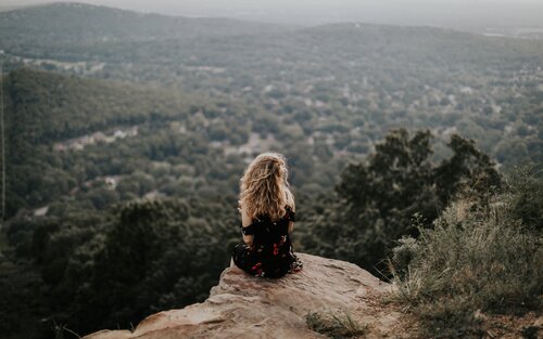 Eine Frau sitzt alleine in der Natur auf einem Aussichtspunkt und schaut runter in den Wald.  | © unsplash