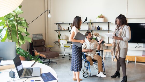 Drei Personen stehend im Büro, wobei eine Person mobilitätseingeschränkt ist. | © Pexels/Kampus