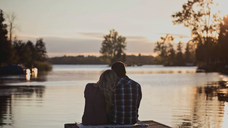 Ein Paar sitzt an einem Steg und kuschelt. | © Unsplash