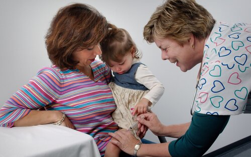 Eine Mutter hält ihr Kind auf dem Arm, während eine Ärztin ihm eine Spritze gibt. | © unsplash