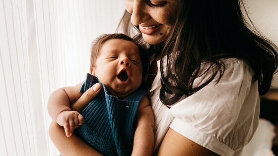 Eine Mutter hält lächelnd ihr Baby im Arm. | © Unsplash