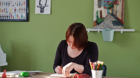Eine Frau sitzt am Schreibtisch und notiert etwas. | © Unsplash