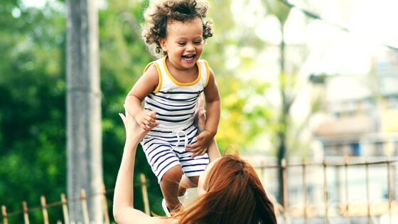 Eine Mutter wirft ihr lachendes Kind in die Luft. | © Unsplash