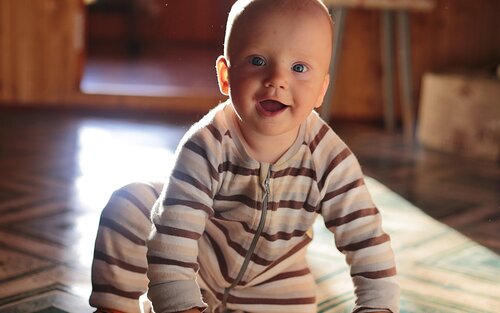 Ein Baby im Strampler krabbelt und lächelt in die Kamera. | © pixabay