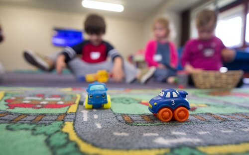 Kinder spielen auf einem Kinderteppich mit Spielzeugautos.  | © unsplash