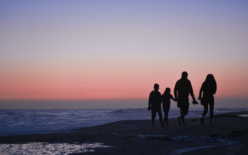Eine vierköpfige Familie spaziert in Dämmerung am Stand. | © unsplash