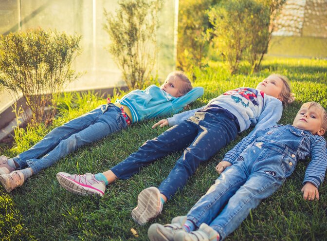 Drei Kinder liegen auf einer Wiese. | © unsplash
