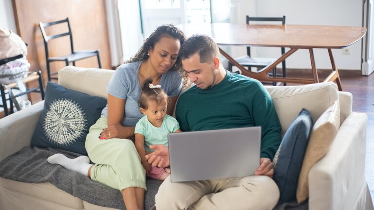 Eltern sitzen mit ihrer kleiner Tochter und einem Laptop auf den Knien auf dem Sofa und informieren sich. | © Pexels / Kampus Production