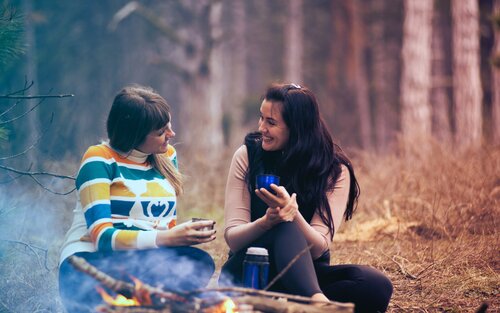 Zwei junge Frauen sitzen im Wald an einem Lagerfeuer und unterhalten sich miteinander. | © pexels