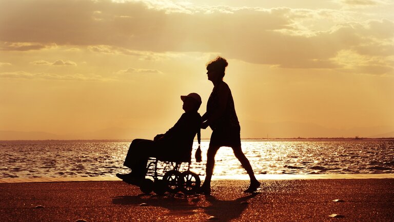 Eine Person im Rollstuhl mit einer Begleiterin am Strand.  | © pixabay