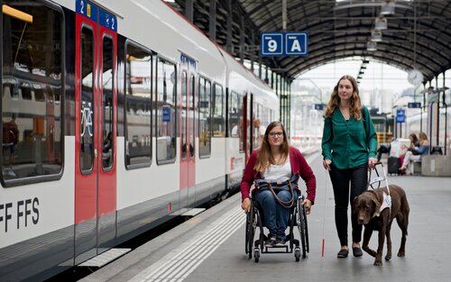 Une voyageuse en fauteuil roulant manuel et une voyageuse aveugle avec son chien guide d'aveugle sur le quai. | © SBB CFF FFS/Flavia Trachsel