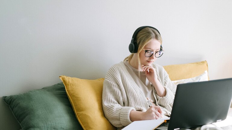 Eine Frau sitzt mit dem Laptop und Kopfhörern bequem auf ihrem Bett und recherchiert im Internet oder beteiligt sich in einem Forum. | © Pexels / Ivan Samkov
