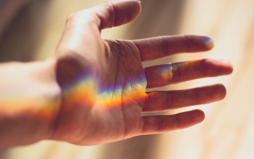 Ausgestreckte Hand, die durch eine Scheibe in Regenbogenfarben beschienen wird. | © pexels