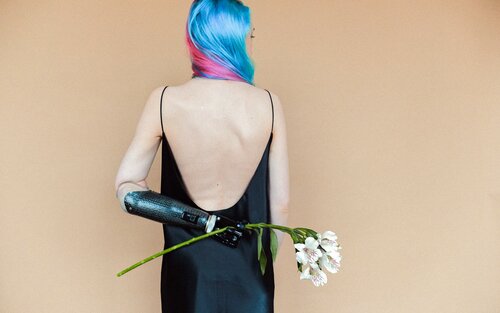 Eine junge Frau hält mit ihrer Armprothese Blumen an ihren Rücken. | © pexels