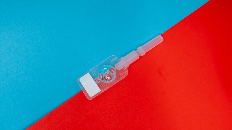 Eine Spritze mit Flüssigkeit gefüllt vor rot-blauem Hintergrund. | © unsplash