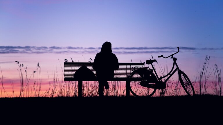 Personne seule assise sur un banc au coucher du soleil | © pixabay