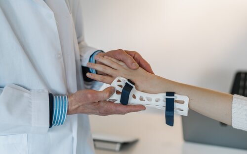 Arzt hilft einer Person beim Anziehen einer Handschiene. | © unsplash