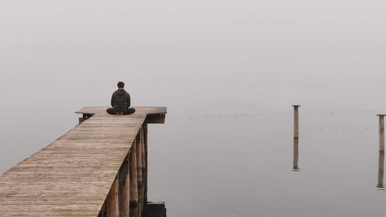 Ein Mann sitzt meditierend auf einem Steg am Meer. | © Pixabay/Patrizia08