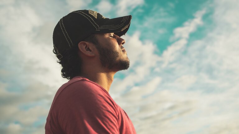 Mann der eine Kappe trägt und mit geschlossenen Augen unter freiem Himmel steht. | © Pexels/Kelvin Valerio