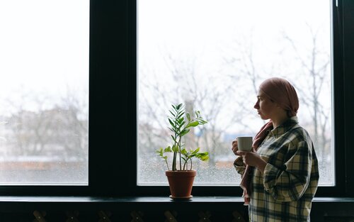 Eine Frau, die wegen ihrer Krebserkrankung ein Kopftuch trägt, schaut nachdenklich in die Ferne und hält dabei eine Kaffeetasse. | © pexels