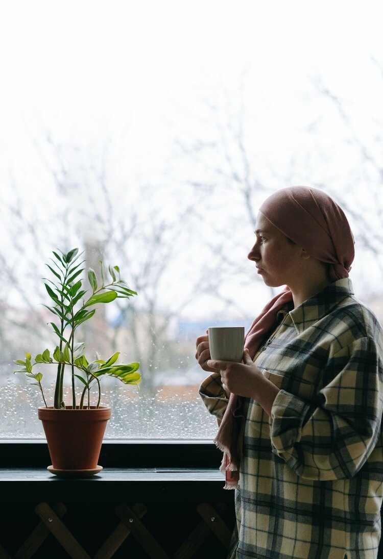 Eine Frau, die wegen ihrer Krebserkrankung ein Kopftuch trägt, schaut nachdenklich in die Ferne und hält dabei eine Kaffeetasse. | © Pexels / Thirdman
