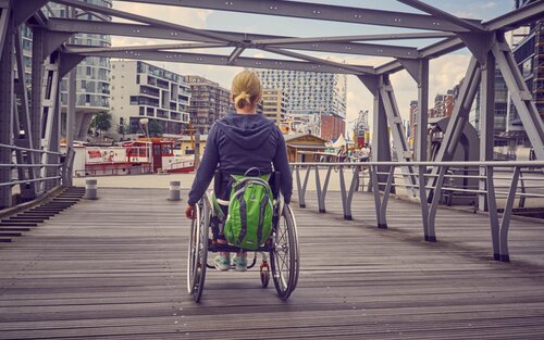 Frau im Rollstuhl, die eine Brücke überquert. | © Gesellschaftsbilder.de